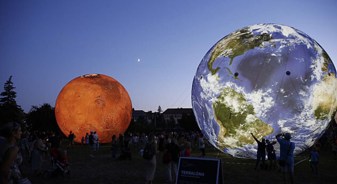 Illuminated Mars and Earth spheres at dusk with visitors